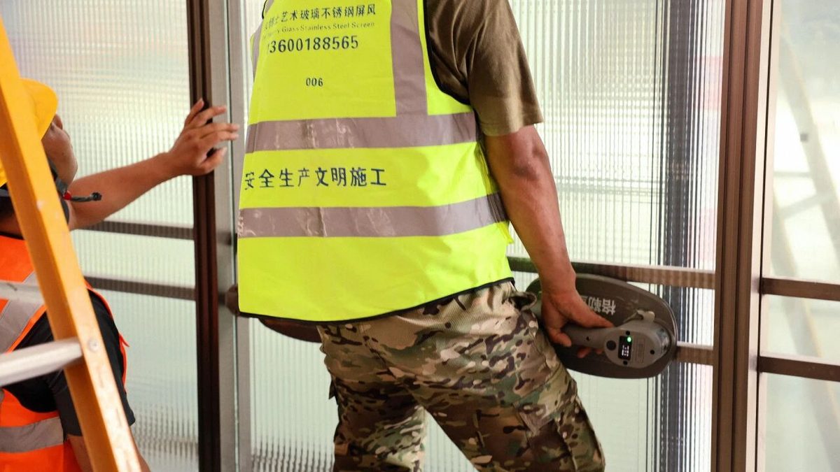 师傅站在梯子上用电动吸盘为玻璃对位
